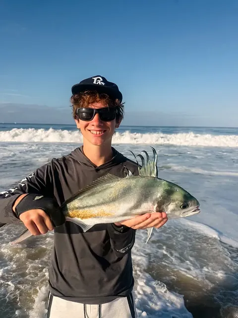 A young angler holding a roosterfish beside the surf on a Tag Cabo Sportfishing outing.